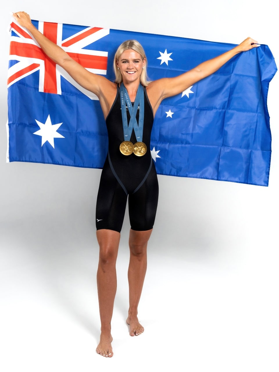 Shayna Jack holding an Australian flag behind her, wearing two Olympic gold medals.